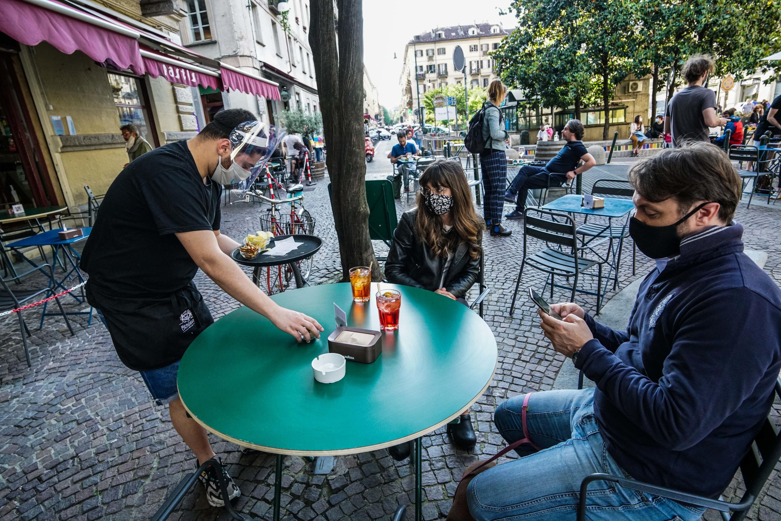 Un cameriere serve da bare con la mascherina e la visiera in un locale del quartiere del Quadrilatero a Torino, 29 maggio 2020.
ANSA/TINO ROMANO