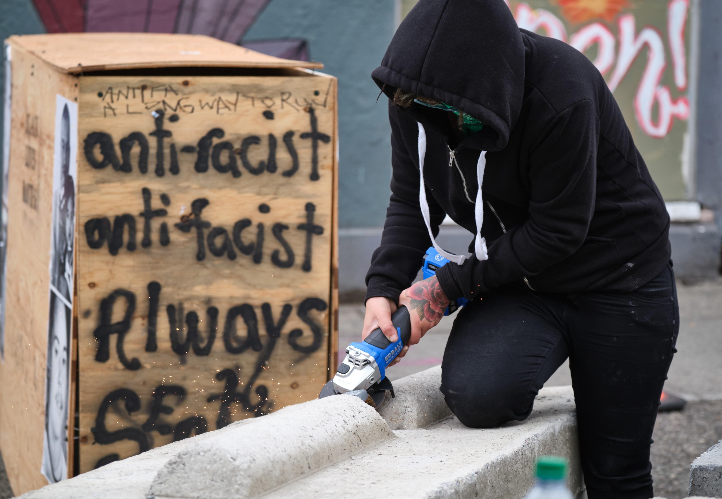 epa08515106 A protestor uses and angle grinder to remove a rebar rung from a concrete barrier, to make it more difficult to remov, in the Capitol Hill Occupied Protest, an area near a precinct abandoned by police where activists continue to protest police brutality and support the Black Lives Matter movement, in Seattle, Washington, USA, 28 June 2020. The city is planning to remove barriers from the area and reoccupy the police station.  EPA/STEPHEN BRASHEAR