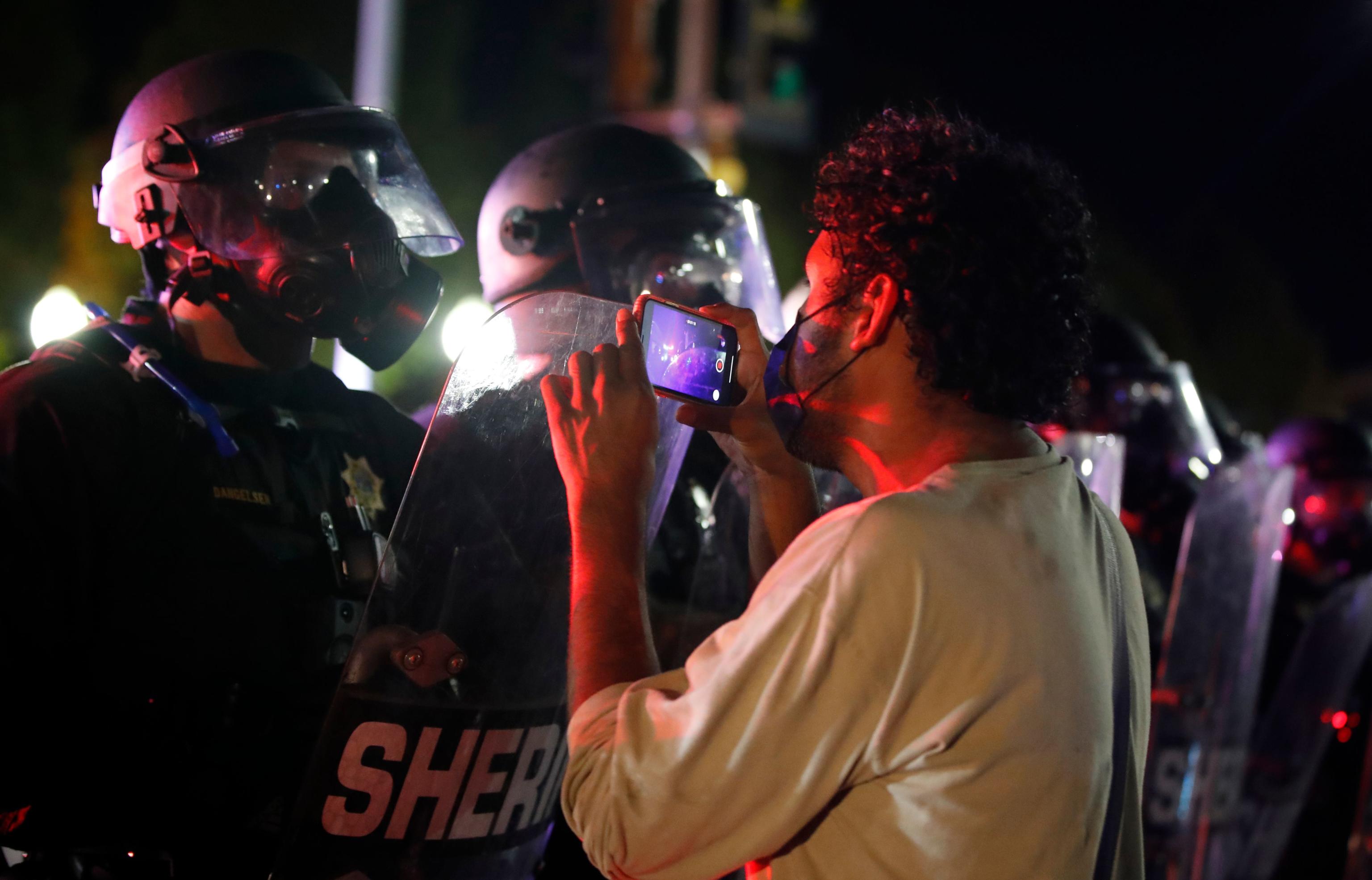 A protestor records a video on his cell phone as he faces off with sheriff's outside the County Courthouse during demonstrations against the shooting of Jacob Blake in Kenosha, Wisconsin on August 25, 2020. - The mother of a black man shot repeatedly in the back by Wisconsin police called August 25 for calm after two nights of violent protests, as her lawyer said it would take a "miracle" for her son to walk again. Expecting another night of demonstrations, Kenosha authorities installed a temporary iron fence in front of the county courthouse, a scene of confrontations between police and protesters the last two nights. (Photo by KAMIL KRZACZYNSKI / AFP)