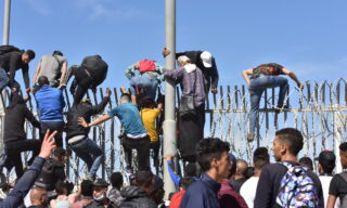 epa09210801 Migrants climb the fence in the northern town of Fnideq in an attempt to cross the border from Morocco to the Spanish enclave of Ceuta, in North Africa 18 May 2021.  In little over 24 hours a total of almost 8,000 people entered into the Spanish city of Ceuta, located in the North African coast, by sea side and hundreds of migrants continue to attempt doing so. The Spanish authorities have deployed the army to patrol on the border separating Ceuta in the Spanish side from the Moroccan side, in a bid to control this latest surge of entry attempts.  EPA/JALAL MORCHIDI