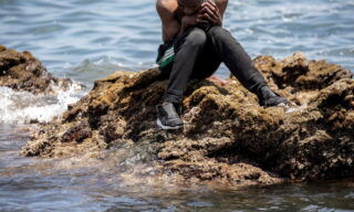 epa09209429 A migrants sits on a rock after crossing the border of Tarajal in Ceuta, Spain, 18 May 2021. On the night of 17 May, a total of 5,000 Moroccan nationals entered into the Spanish city of Ceuta, loacted in the North African coast, by sea side and hundreds of migrants continue to attempt doing so. The Spanish authorities have deployed the army to patrol on the border separating Ceuta in the Spanish side from the Moroccan side, in a bid to control this latest surge of entry attempts.  EPA/BRAIS LORENZO