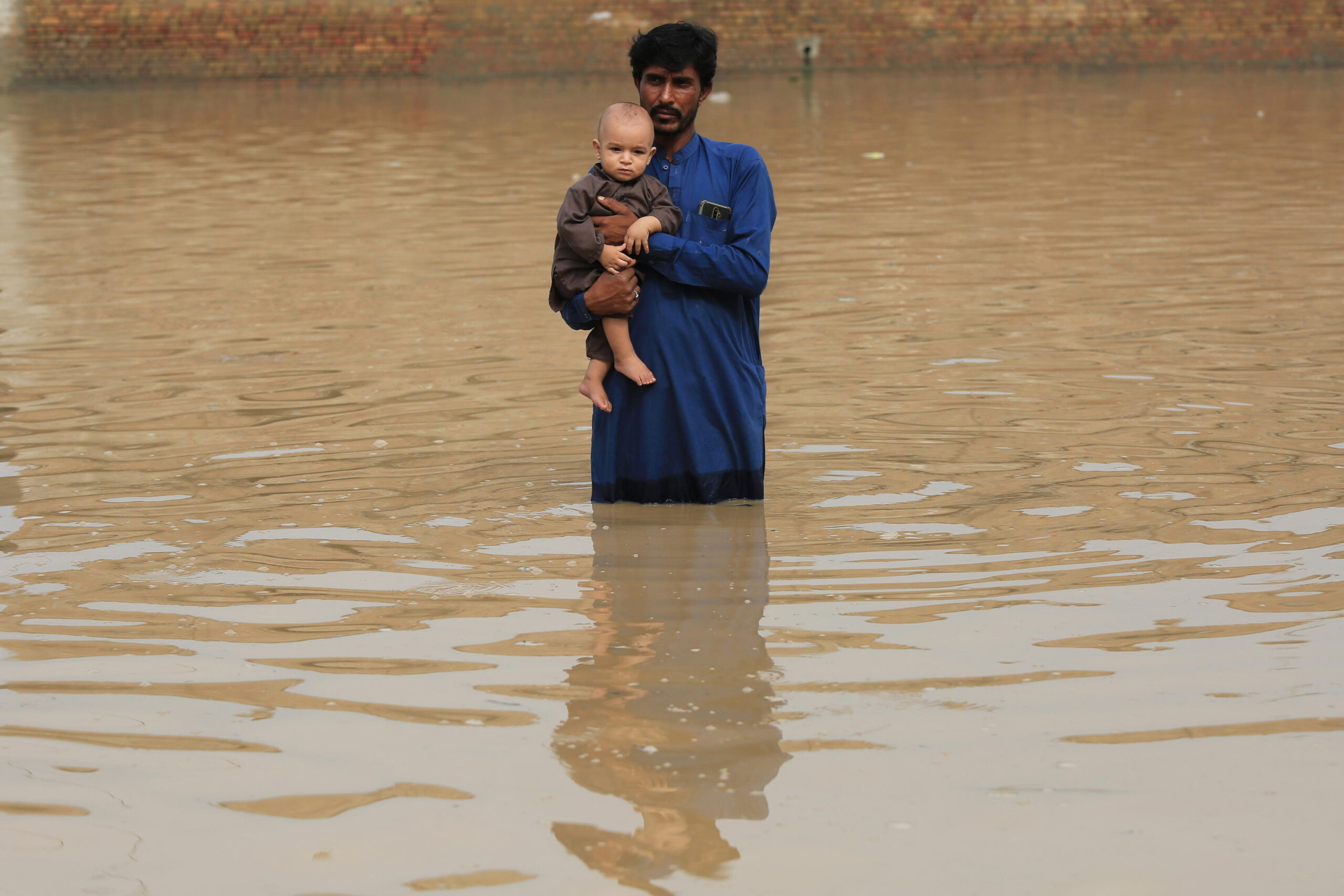 epa10141288 A man holding a baby wades through a flooded area following heavy rains in Charsadda District, Khyber Pakhtunkhwa province, Pakistan, 27 August 2022. According to the National Disaster Management Authority (NDMA) on 26 August, flash floods triggered by heavy monsoon rains have killed over 900 people across Pakistan since mid-June 2022. More than 33 million people have been affected by floods, the country's climate change minister said.  EPA/ARSHAD ARBAB
