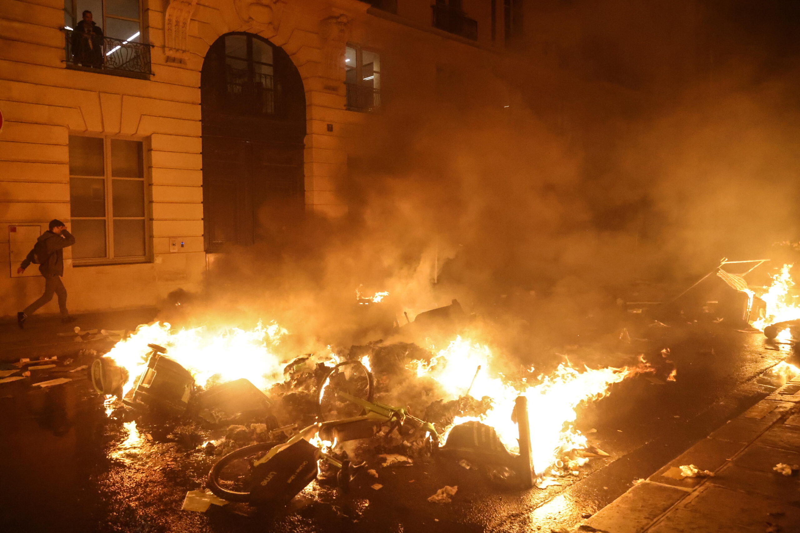 epa10527532 A person walks past a fire after a demonstration near the National Assembly after the French National Assembly vote on the government's proposed pension reform law, in Paris, France, 16 March 2023. People demonstrated outside the French Parliament after French Prime Minister Borne invoked the controversial Article 49 paragraph 3 (49.3) of the Constitution to pass the pension reform law that would raise the retirement age from 62 to 64 by 2030 after the Senate voted in favor.  EPA/Mohammed Badra