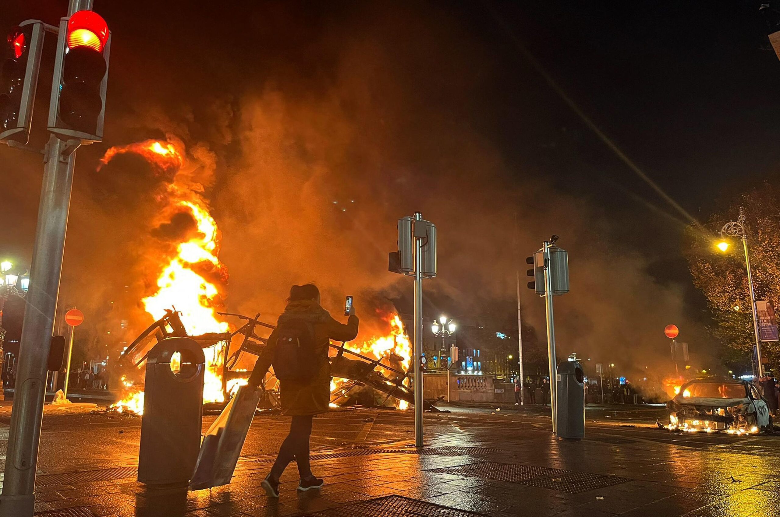 Flames rise from the car and a bus, set alight at the junction of Bachelors Walk and the O'Connell Bridge, in Dublin on November 23, 2023, as people took to the streets following the stabbings earlier in the day. Protesters in Dublin on Thursday torched a car and fought police, an AFP journalist reported, after three children were injured in a suspected school stabbing that social media rumours attributed to a foreign national. (Photo by Peter MURPHY / AFP)