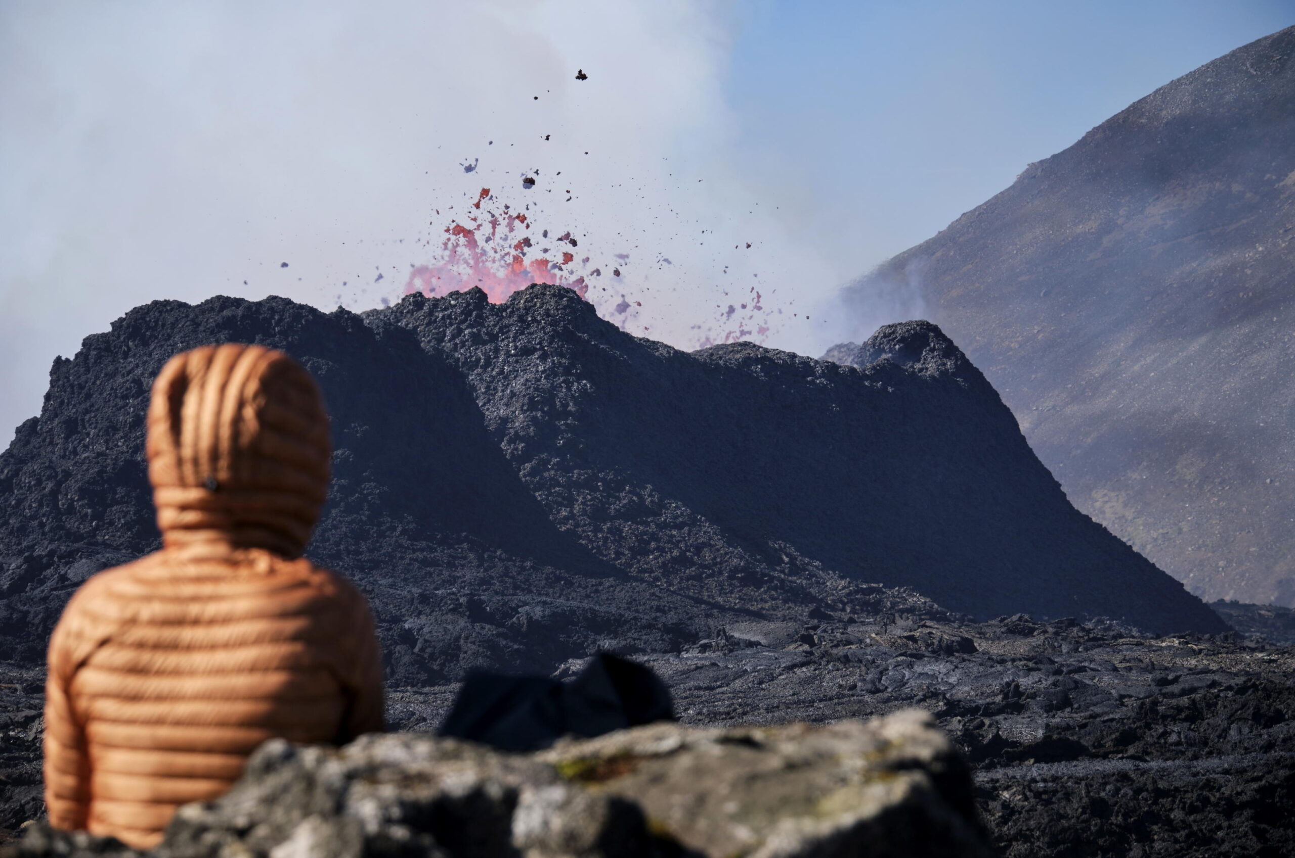 epa10743798 A person looks at spewing lava and billowing smoke during an ongoing volcanic eruption at Litli Hrutur on the Reykjanes peninsula, some 30km south of the capital Reykjavik, Iceland, 13 July 2023. The intensity of the eruption by Litli-Hrutur mountain has 'decreased dramatically' since it started on 10 July 2023, with around 300 earthquakes recorded (mostly below 2.0 in magnitude) on the Reykjanes Peninsula, a region known for its sweeping lava fields. The Icelandic Meteorological Office (IMO) said that due to the ongoing eruption near Litli-Hrutur, volcanic gas pollution was expected from the eruption area along with smoke from burning vegetation. The eruption is occurring in an uninhabited area and it posed no immediate dangers to infrastructure, IMO added.  EPA/ANTON BRINK