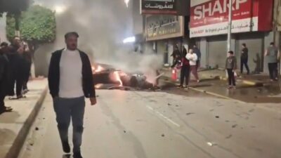 Dettaglio dei detriti di un missile caduti in una strada del centro di Irbid, Giordania: passanti e bambini osservano i resti fumanti sull'asfalto.