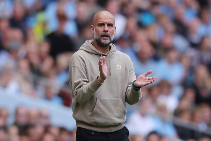 Pep Guardiola durante una conferenza stampa, con espressione seria e concentrata