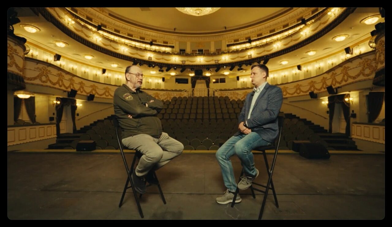 Fotogramma del documentario «Свидетели»: Rangeloni intervista Vladislav Telichko, presentato come ex viceministro ucraino dell’MNS con diploma da artificiere, all’interno del teatro drammatico di Mariupol ricostruito.